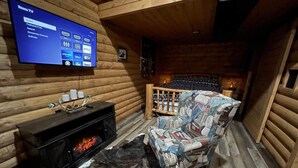 L’intérieur d’une cabane en rondins, avec une cheminée, un téléviseur fixé au mur et un fauteuil à motifs.