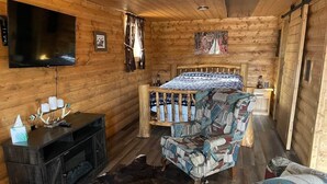 L’intérieur d’une cabane en rondins, avec un lit, un téléviseur, un meuble de rangement en bois et des meubles aux motifs décoratifs.