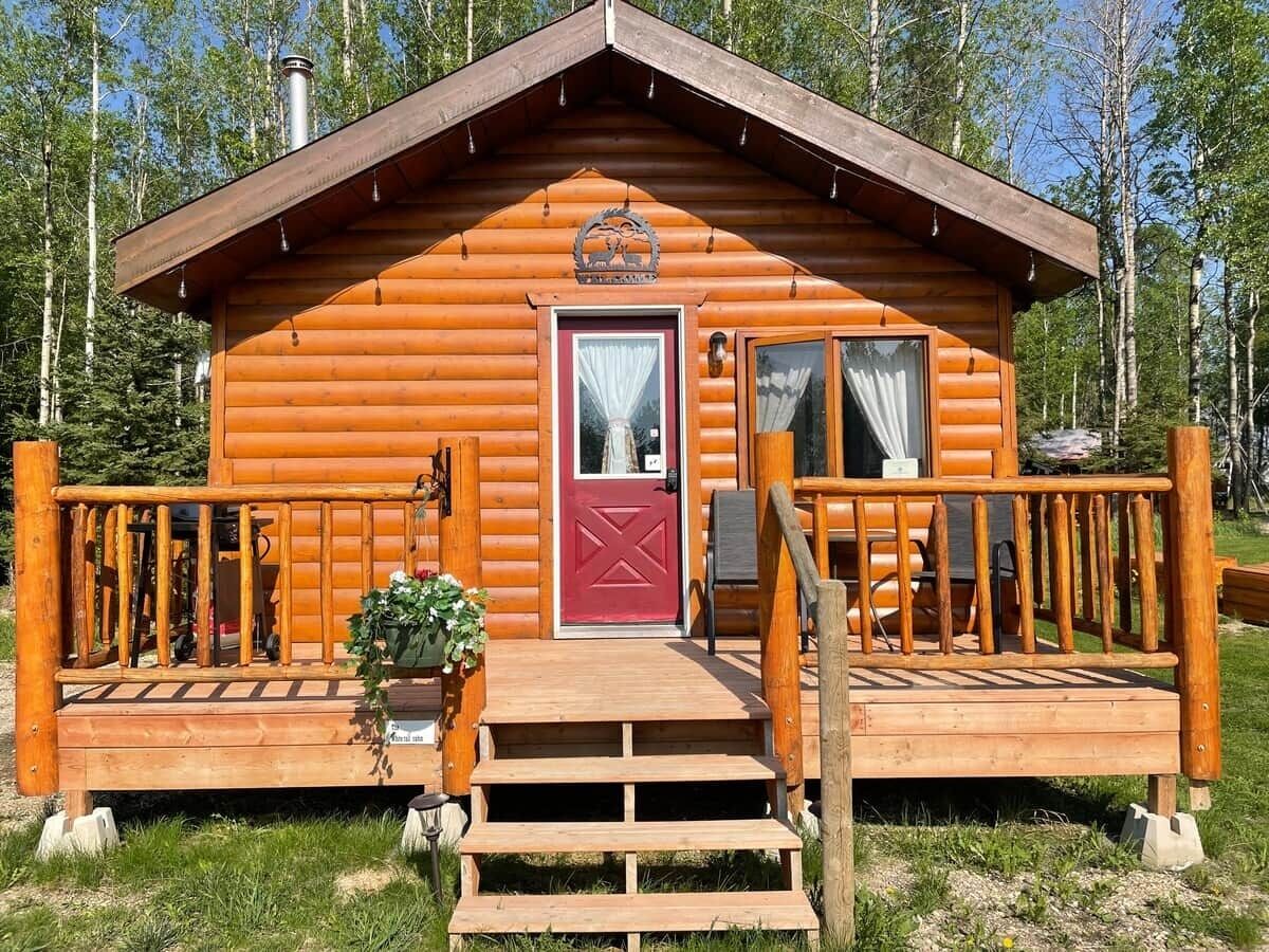 A wooden cabin with a red door, a small porch with steps, and a wooden railing.