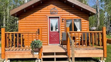 A wooden cabin with a red door, a small porch with steps, and a wooden railing.
