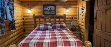 Een slaapkamer in een houten blokhut met een geruite sprei, een foto boven het bed en een houten hoofdbord.