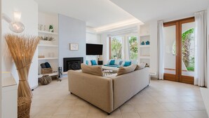 Een moderne woonkamer met een bank, televisie, open haard en grote ramen.