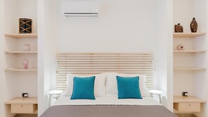 Een slaapkamer met een bed, twee nachtkastjes, een wandairconditioner en planken met decoratieve objecten.