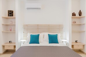 A bedroom with a bed, two bedside tables, a nightstand, a wall-mounted air conditioner, and shelves with decorative items. - Villa Botanica, relax e privacy (ALCAMO)
