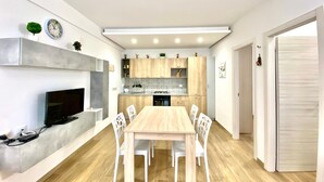 Cuina moderna amb armaris de fusta, forn integrat i zona de menjador amb taula de fusta i cadires blanques.