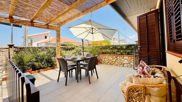 Un porxo exterior cobert amb una taula, cadires i un gran parasol.