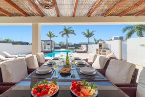 A dining table set for two with a view of a pool and palm trees. - Villa Lorena by Villa Plus (Montaña Roja)