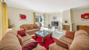 A spacious living room with a sofa set, a glass coffee table, and a fireplace. - Villa Caly by Villa Plus (Olhos de Água)