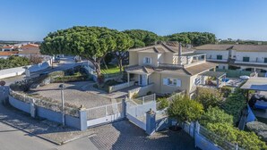 A two-story building with a tiled roof, surrounded by a white fence and a large tree. - Villa Caly by Villa Plus (Olhos de Água)