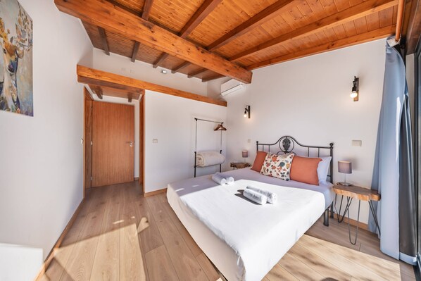 Quarto com teto de madeira, cama com almofadas, mesa de cabeceira e luminária na parede.