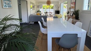 A modern kitchen with a white countertop, a dining area with a white table and chairs, and a large window providing a view of the outdoors.