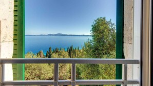 Blick durch ein Fenster mit weißem Rahmen auf ein Gewässer mit weiter Küste und Bäumen.