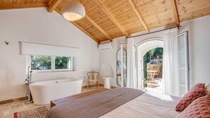 Ein Schlafzimmer mit einem großen Bett, einer Badewanne, einem Fenster und einem Außenbereich mit Tisch und Stühlen.