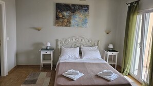 Ein Schlafzimmer mit einem Bett, zwei Nachttischen, einer Wandlampe, einem Gemälde und einem Fenster mit Vorhängen.