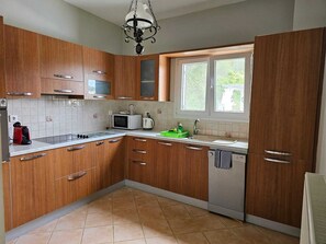 A kitchen with wooden cabinets, a microwave, a kettle, and a window with a view. - Villa Armonia A by Corfu Stay Solutions, Villa (Corfu)
