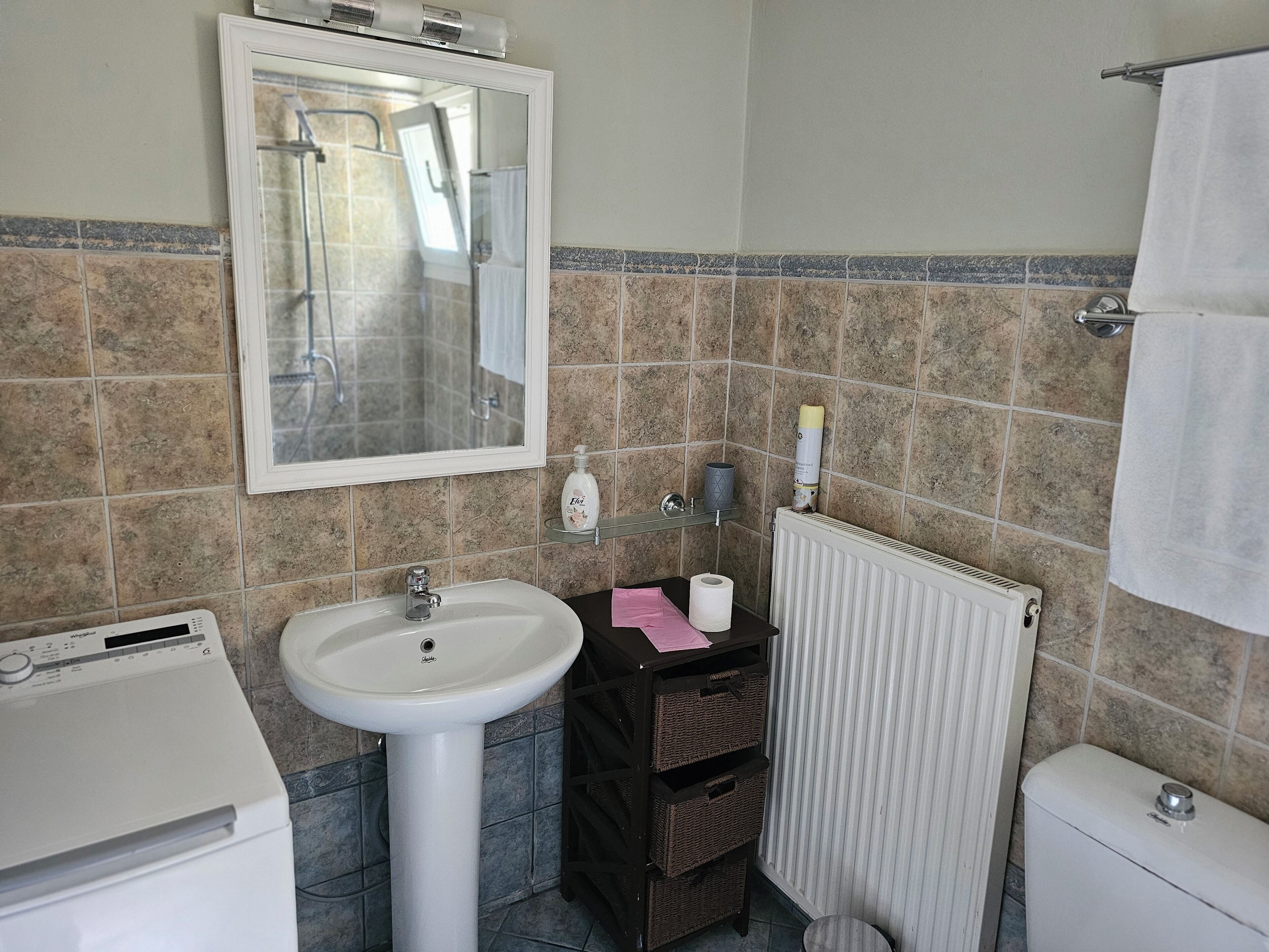 Un bagno con lavandino bianco, specchio, water e termosifone.