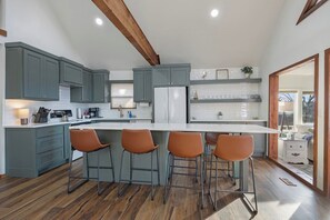 A modern kitchen with grey cabinets, a white island with bar stools, and wooden beams on the ceiling.