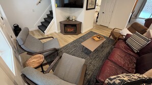 A living room with a fireplace, grey and brown sofas, a TV mounted on the wall, and a staircase leading to another level.