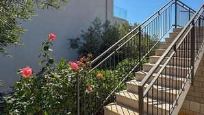A staircase with beige steps and black railings, surrounded by greenery and pink flowers.