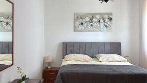A bedroom with a bed, a nightstand, a lamp, a mirror, and a floral painting on the wall.