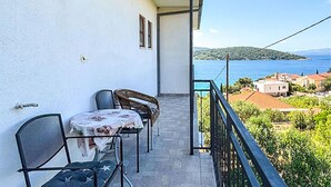 A balcony with a table and chairs, overlooking a coastal town and sea.