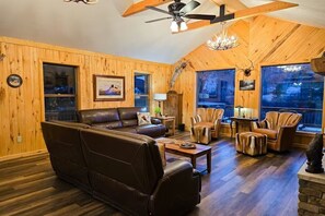 A cozy living room with a large leather sofa, wooden walls, and a ceiling fan. - The Rivers Edge w/Hot Tub Near Wolf Creek (South Fork)