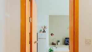 A hallway leading to a living area with a white refrigerator, a TV, and a plant. - Cozy One-Bedroom Penthouse in Sliema (Tas-Sliema)