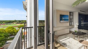 Ein modernes Wohnzimmer mit einem großen Fenster, einem Flachbildfernseher und Blick auf ein Sportfeld.