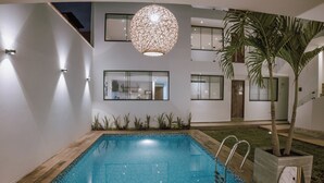 Een modern zwembadgedeelte met een houten terras, een hangende bolvormige lamp en een potpalm.