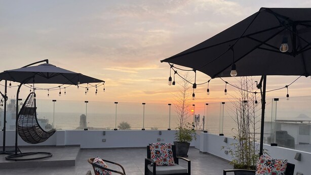Een terras op het dak met zitplaatsen, parasols en lichtslingers.