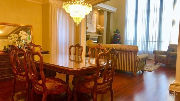 Un comedor con mesa y sillas de madera, una araña y un sofá al fondo.