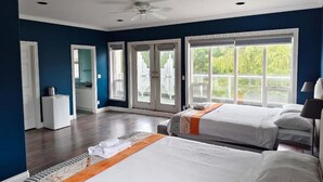 Habitación de hotel con dos camas, ventilador de techo y ventanas amplias con vistas a zonas verdes.