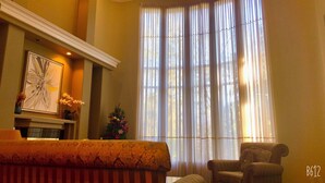 Habitación con chimenea, un cuadro abstracto enmarco, un pequeño árbol de Navidad y un amplio ventanal con cortinas traslúcidas.