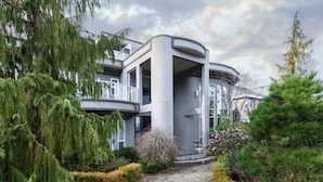 Un edificio moderno de varios pisos con fachada curva, rodeado de vegetación exuberante y un camino de adoquines.