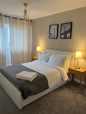 A neatly made bed with white linens and a gray throw blanket, two bedside lamps, and two framed pictures on the wall. - 2-bed Apart in the Heart of Aberdeen (Aberdeen)