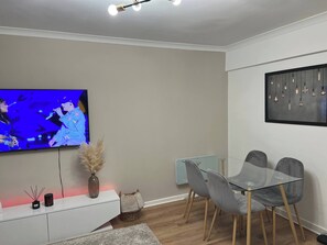 A modern living room with a flat-screen TV, a glass dining table with grey chairs, a white console, and a wall-mounted light fixture. - 2-bed Apart in the Heart of Aberdeen (Aberdeen)