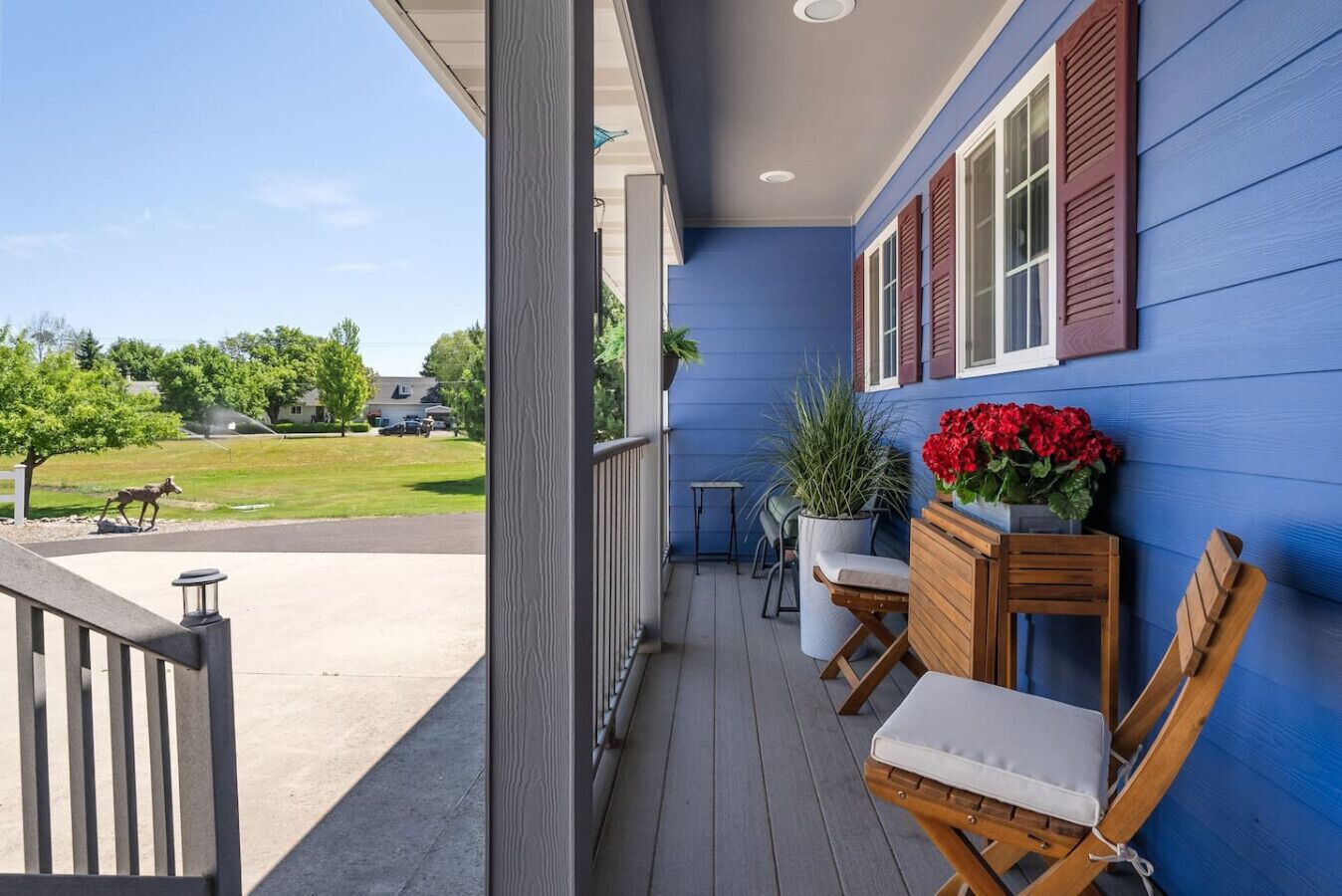 Eine überdachte Veranda mit blauer Fassade, Holzstühlen, einem Tisch und Kübelpflanzen.