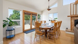 Un coin repas avec une table et des chaises en bois, une plante en pot et, à travers des portes vitrées, une vue sur une terrasse extérieure.