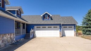 Une maison à deux étages, avec des fondations en pierre, une façade bleue et un toit gris. Elle possède deux portes de garage et un porche avant couvert, accessible par quelques marches.