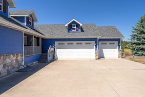 Une maison à deux étages, avec des fondations en pierre, une façade bleue et un toit gris. Elle possède deux portes de garage et un porche avant couvert, accessible par quelques marches.