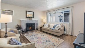 Un salon avec une cheminée, un canapé, une table basse et une grande fenêtre équipée de stores.