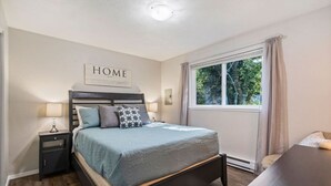 Une chambre à coucher avec un lit, des tables de chevet, une fenêtre et un panneau décoratif portant l’inscription « HOME » sur le mur.