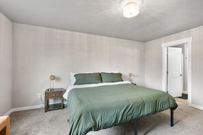 Un dormitorio con cama, mesitas de noche, lámpara y puerta.