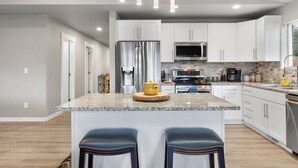 A modern kitchen with white cabinets, stainless steel appliances, granite countertops, and pendant lighting. - Near Perry, Near Perfect (Spokane)
