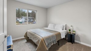 A bedroom with a bed, a nightstand, a window, and a view of a house outside. - Near Perry, Near Perfect (Spokane)