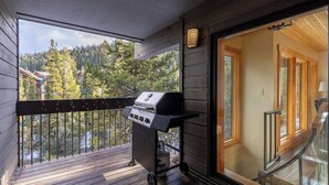 Un balcone con una griglia, vista su una foresta e interni in legno.