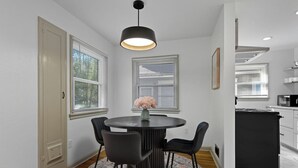 Un coin repas comprenant une table ronde, quatre chaises, un vase avec des fleurs et un luminaire suspendu.