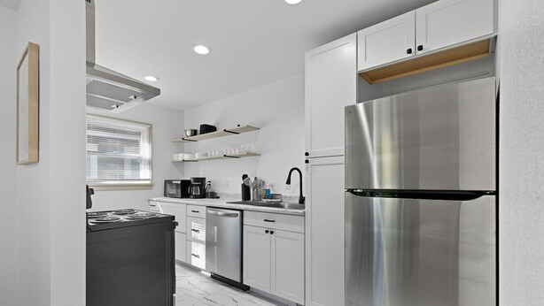 Une cuisine moderne dotée d’appareils électroménagers en acier inoxydable, de meubles blancs et d’un sol en marbre.