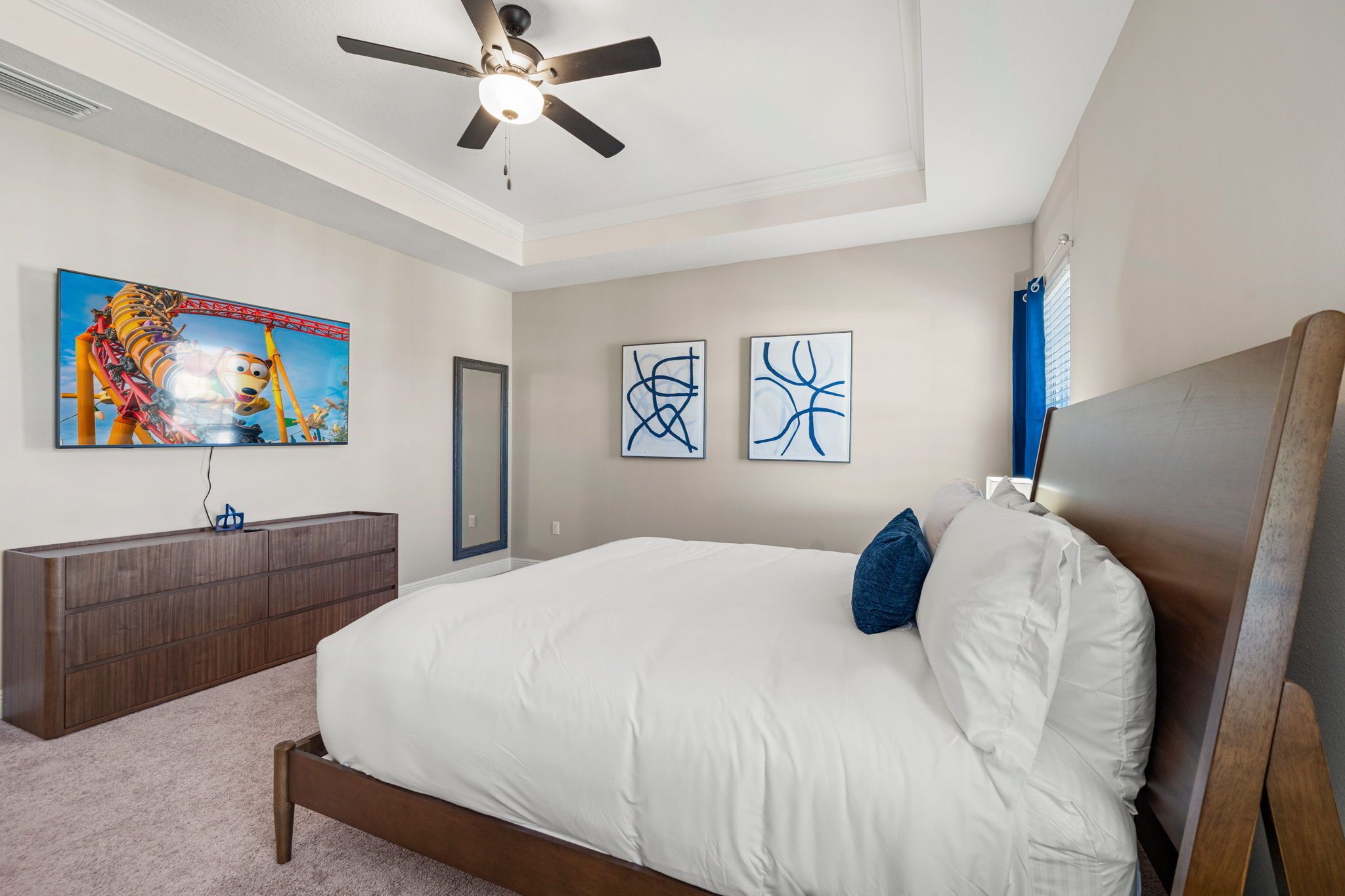 Quarto com cama, ventilador de teto, penteadeira e televisão na parede.
