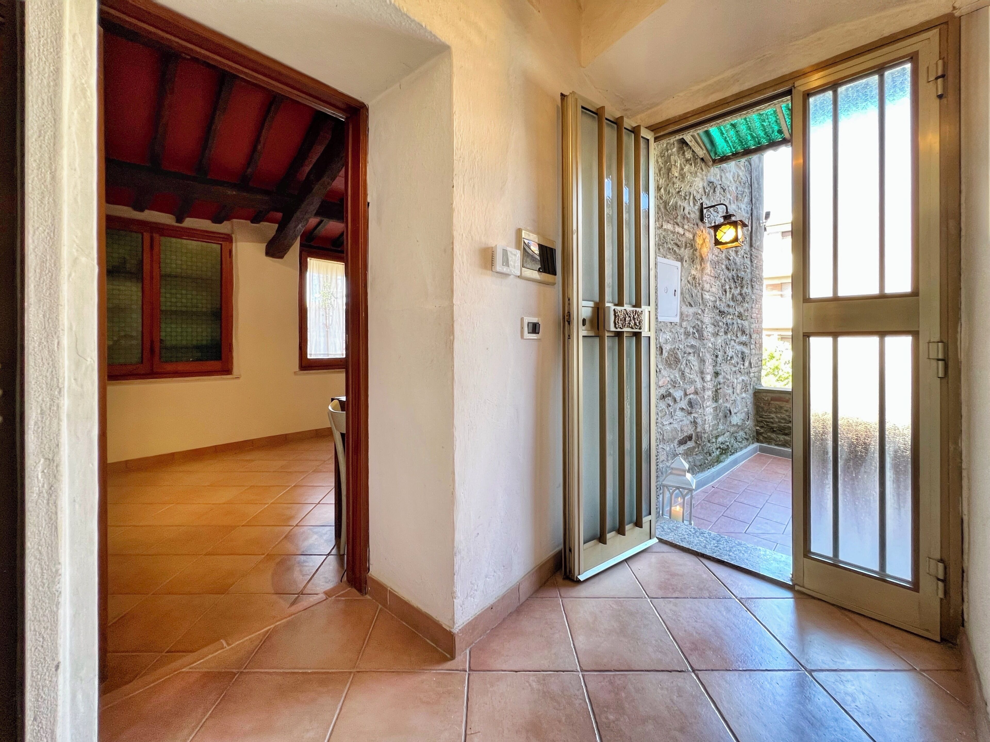 A hallway with a tiled floor, a wooden door, and a glass door leading outside.